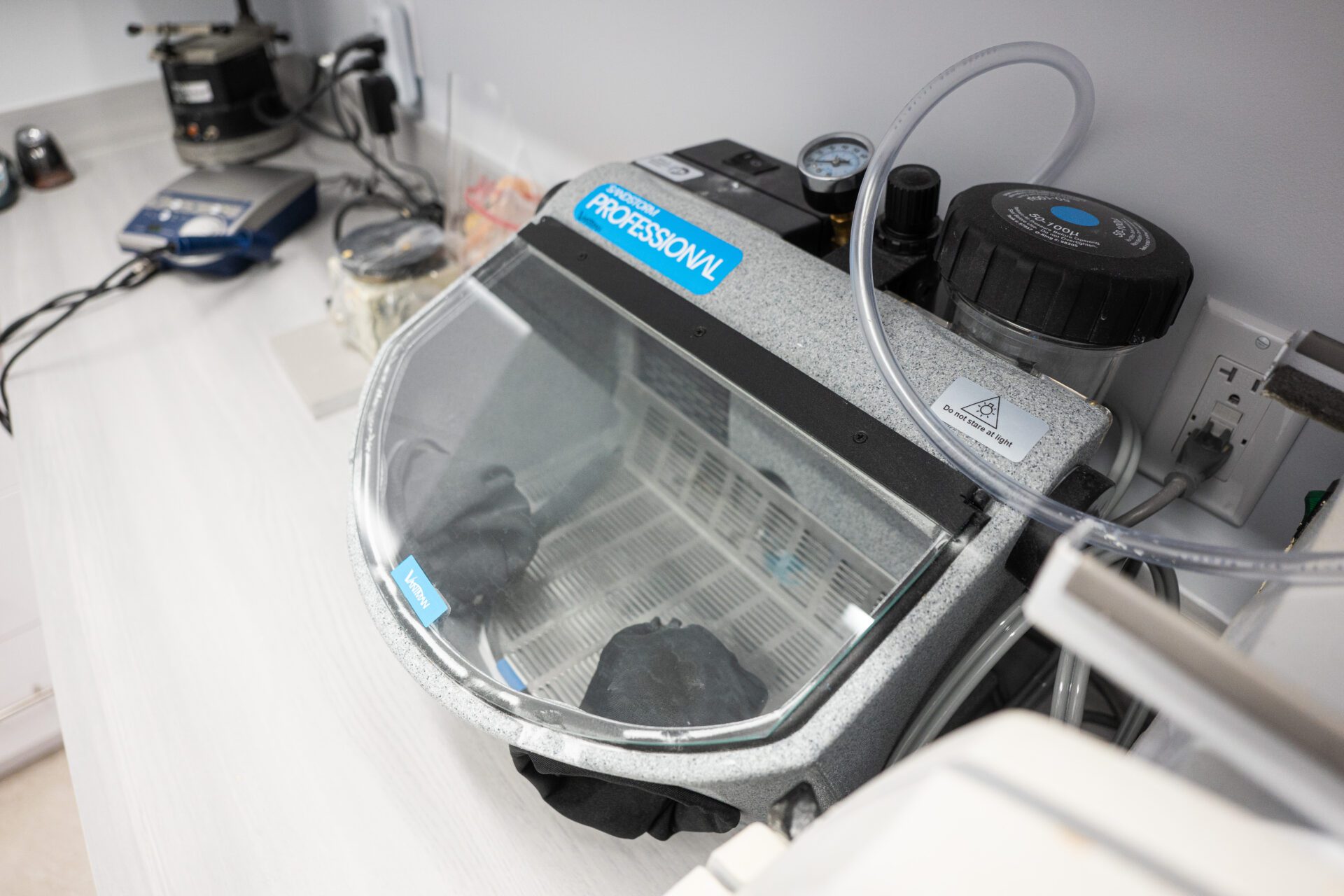 A Vaniman Sandstorm Professional abrasive sandblaster unit sitting on a white dental laboratory countertop with integrated gloves and a clear shield.