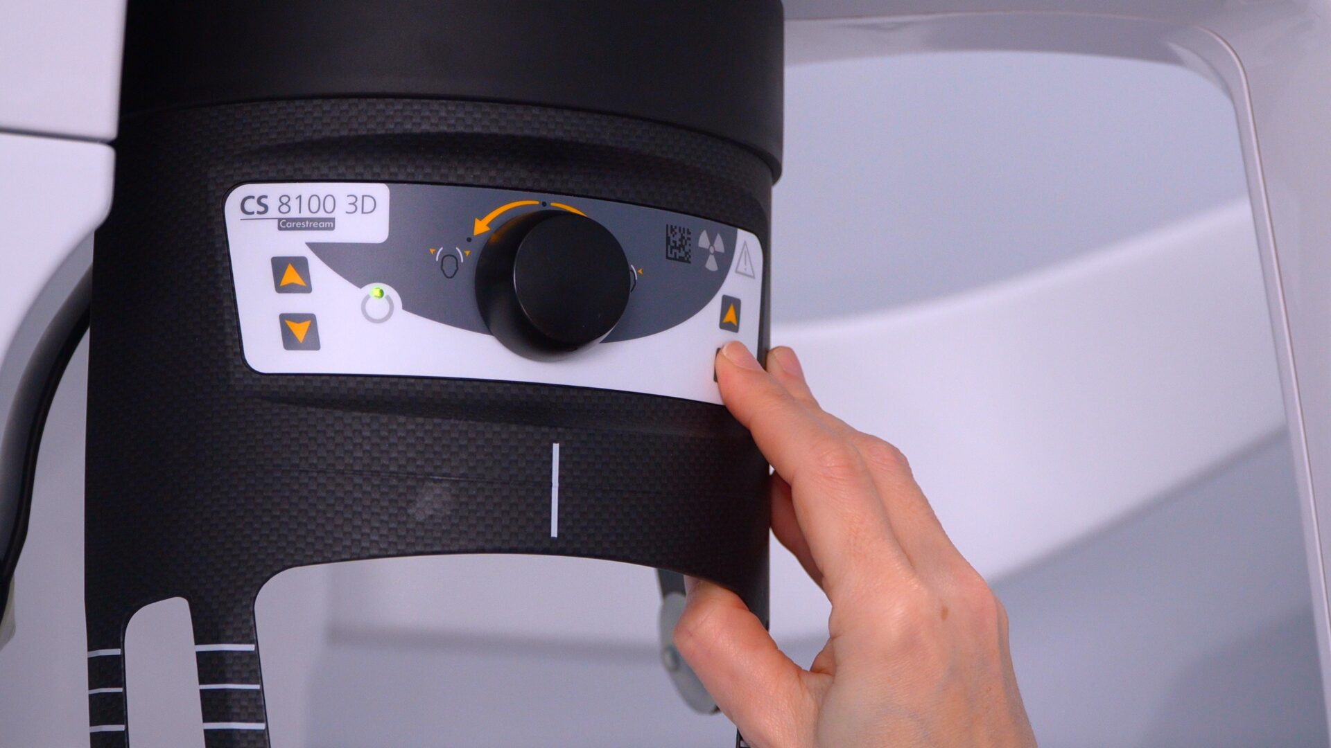 A close-up view of a technician's hand adjusting the control panel on a Carestream CS 8100 3D dental imaging machine.