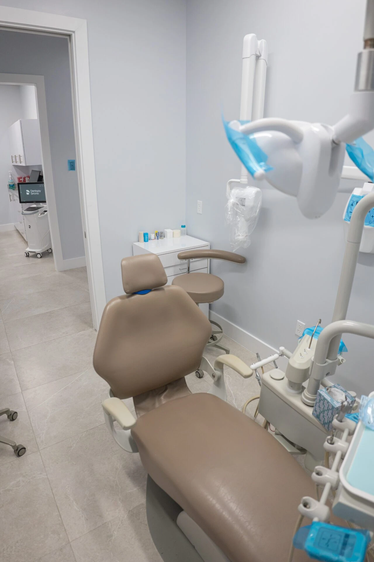 A clean and modern dental operatory featuring a tan leather patient chair, specialized dental tools, and advanced technology in a professional clinic setting.