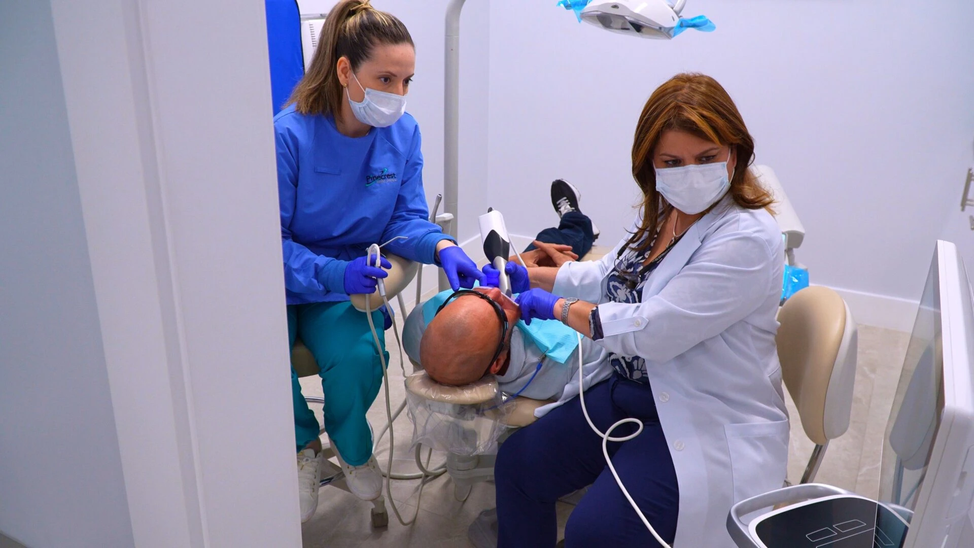 A dentist using a high-tech intraoral scanner on a patient in a modern dental office, assisted by a dental professional.