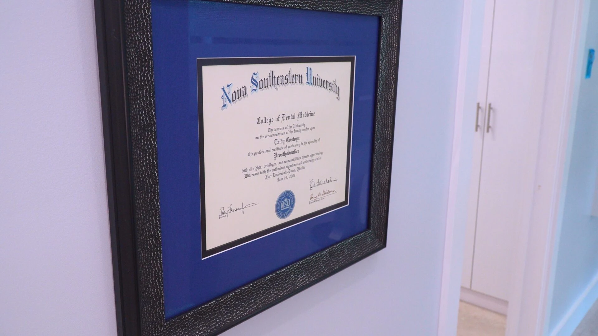 Framed postdoctoral certificate in Prosthodontics from Nova Southeastern University College of Dental Medicine hanging on a wall.