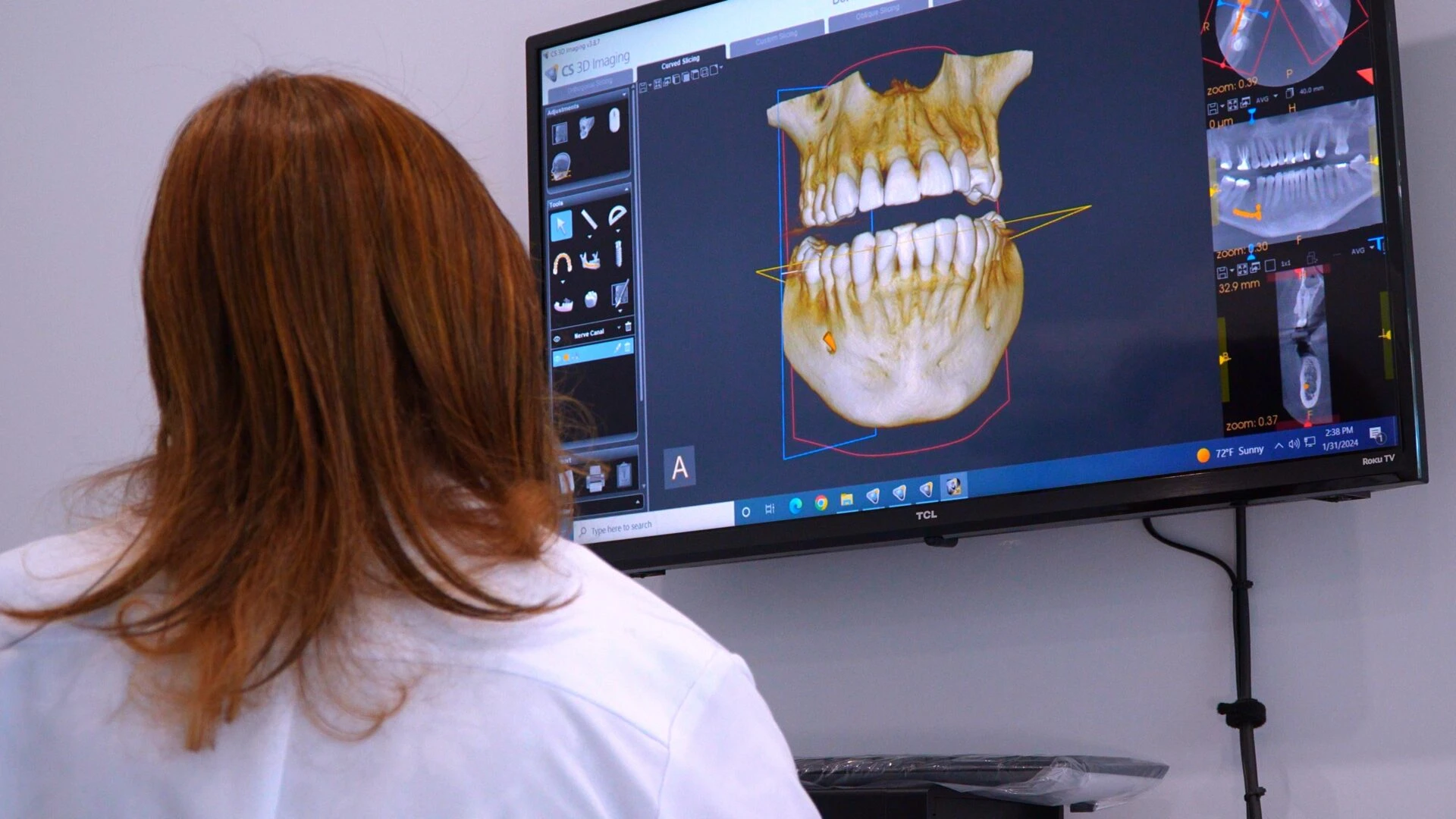 A female dental professional in a white lab coat viewing a high-resolution 3D scan of a human jaw and teeth on a large monitor.
