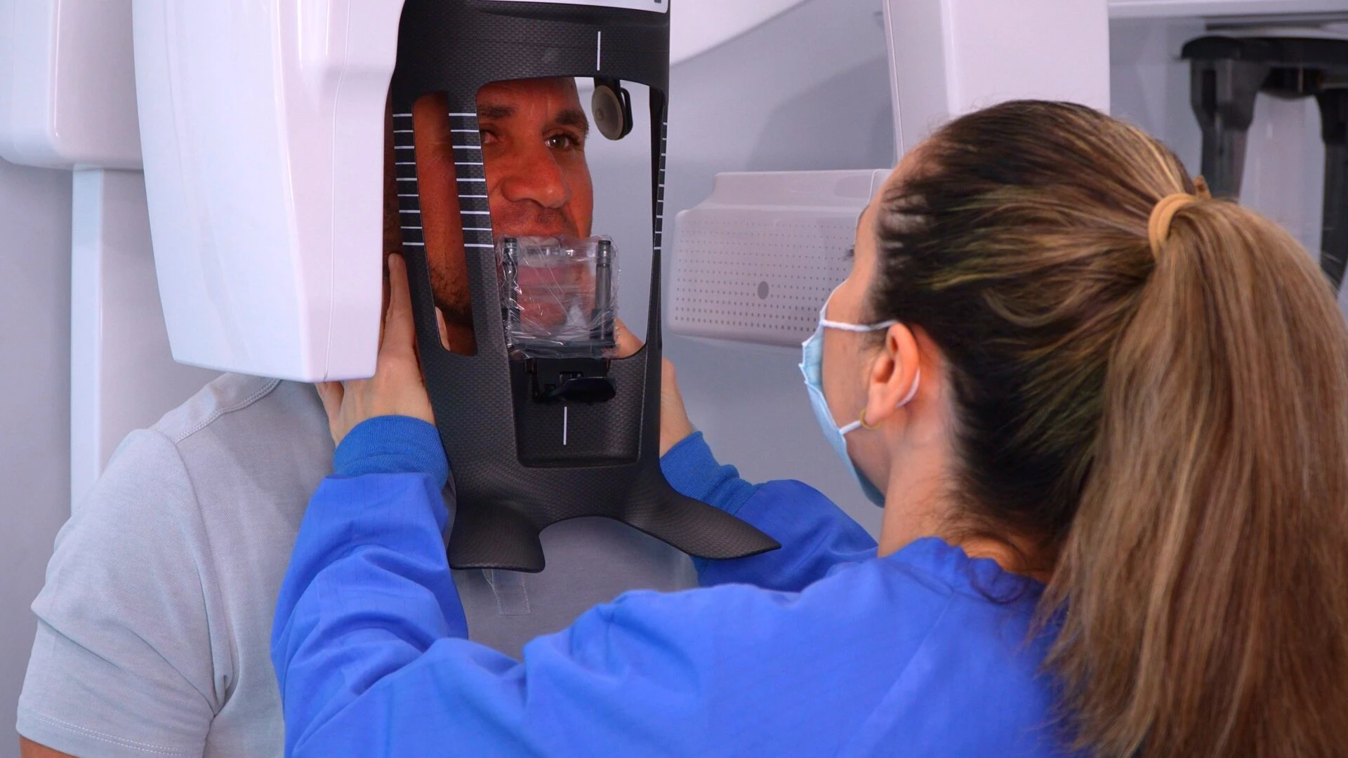 A professional female dentist wearing a white lab coat standing in front of high-tech dental imaging equipment in a clinic.